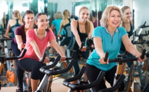 Women of diverse ages enjoy a group cycling class in a bright fitness studio, promoting camaraderie and health.